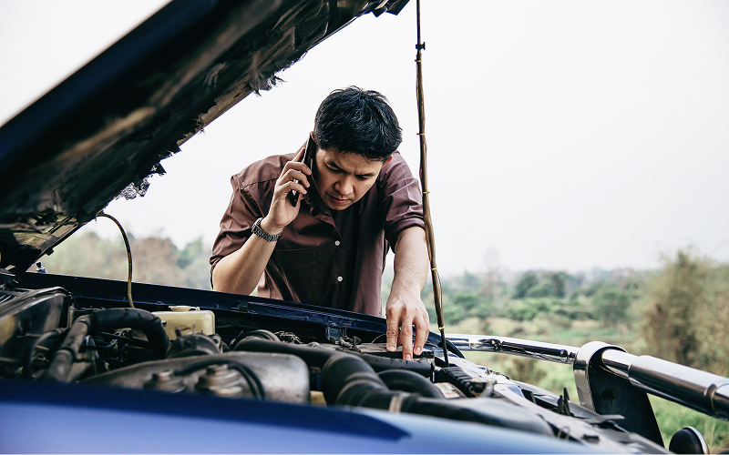 Man-calling-for-assistance-beside-broken-down-rental-car-engine